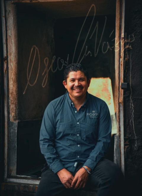 Master distiller Óscar Vázquez Camarena seated at the stone oven doorway at the Mosto distillery in Jesús María, Jalisco, with his signature across the image
